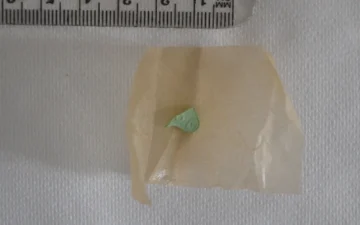 Mały zielony fragment tabletki na papierze, obok linijki